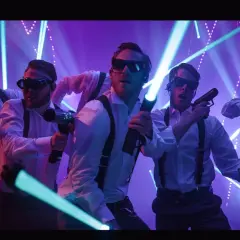 Gruppo di amici in camicia bianca e bretelle, occhiali da sole e pistole laser, pronti per un addio celibato o nubilato in un tripudio di luci.