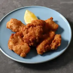 Chrupiące kawałki kurczaka karaage na niebieskim talerzu, ozdobione ćwiartką cytryny. Idealna przekąska.