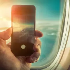 Dłoń trzyma smartfon, którym fotografuje chmury z okna samolotu. Czy w samolocie można używać telefonu? Tak, do robienia zdjęć!