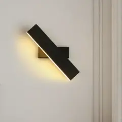 Moderna lámpara de pared negra con luz LED cálida, ilumina un rincón acogedor junto a un jarrón con flores secas.