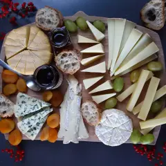 Un tagliere ricco di formaggio di capra francese, accompagnato da pane croccante, uva, albicocche secche e marmellata.