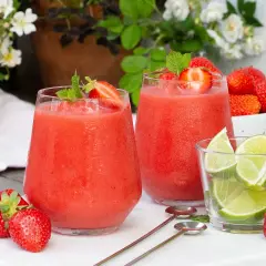 Två frostiga jordgubbsdaiquiri-drinkar med mynta och jordgubbar, serverade med limeklyftor och färska jordgubbar.