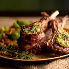 Costillas de cordero asadas con pesto y romero, acompañadas de verduras. Un plato de cordero para recetas gourmet.