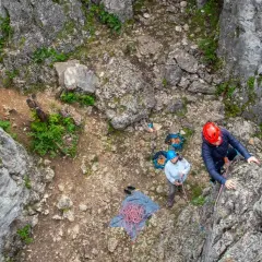 Wspinaczka po skale. Dwie osoby w kaskach przygotowują się do wspinaczki, liny i sprzęt leżą na ziemi.