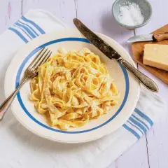Ein Teller cremiger Fettuccine, bestreut mit schwarzem Pfeffer, daneben ein Stück Parmesan und Salz.