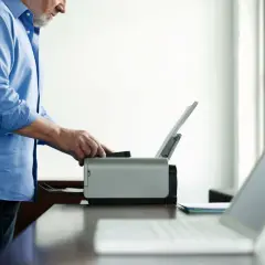 Mężczyzna w niebieskiej koszuli próbuje uruchomić drukarkę w trybie offline. Obok leży laptop.