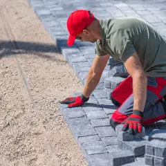 Pracownik układa kostkę brukową, dbając o detale. Poznaj ceny układania kostki brukowej i stwórz wymarzoną nawierzchnię.