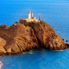 Faro en un acantilado rocoso con el mar azul de fondo. Un camino serpentea hacia la cima. ¡Un lugar perfecto para ver Cabo de Gata!