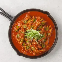 Kurczak w sosie gochujang, ozdobiony zieloną cebulką i sezamem, podany w żeliwnej patelni.