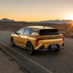 Un coche hatchback amarillo brillante recorre una carretera desierta al atardecer, con las montañas al fondo.