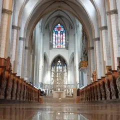 Blick durch das Kirchenschiff des Augsburger Doms mit seinen kunstvoll geschnitzten Holzbänken und dem farbenprächtigen Chorfenster.