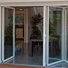 Puertas de cristales plegables que abren a un comedor interior con plantas y una mesa.