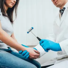 Neurolog w białym kitlu bada pacjentkę młoteczkiem neurologicznym. To dowód, że szuka się najlepszego neurologa w Polsce.