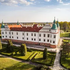 Zamek w Baranowie Sandomierskim, biała rezydencja z czerwonym dachem i zielonymi wieżyczkami, otoczona zadbanym ogrodem.