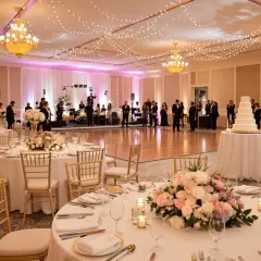 Elegancka sala weselna z oświetleniem, stołami i tortem.