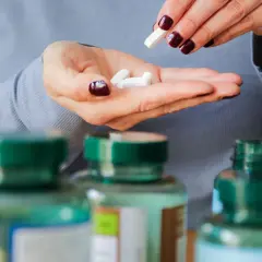 Frau nimmt weiße Kapseln aus der Hand, um die 5-HTP-Wirkung zu erfahren.