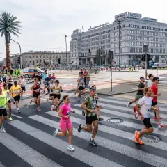 Uczestnicy biegu na ulicach Warszawy, biegacze przekraczają pasy. Biegi Polska to emocje i sport.