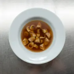 Eine Schüssel mit dampfendem Tortellini in Brodo auf einem metallischen Hintergrund.