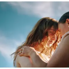 Due donne si abbracciano con dolcezza, un'immagine che evoca il vero amore platonico, significato di profonda connessione spirituale sotto un cielo azzurro.