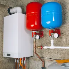 Nowoczesny biały kocioł gazowy z dwoma zbiornikami przeponowymi (czerwonym i niebieskim) oraz instalacją hydrauliczną.