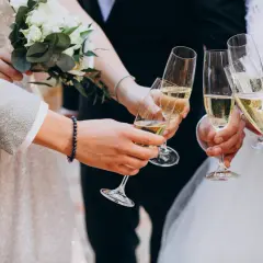 Para młoda i goście wznoszą toast kieliszkami szampana. Wino na wesele to symbol radości i celebracji.