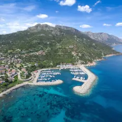 Baunei: un porto turistico con barche ormeggiate, case colorate e montagne verdi che si tuffano nel mare cristallino. Le spiagge vicine invitano al relax.