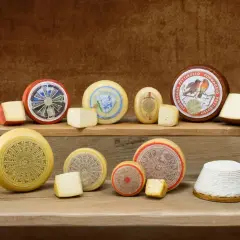 Varietà di formaggi spalmabili per dolci, disposti su assi di legno. Alcuni sono interi, altri tagliati a spicchi.