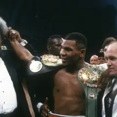 Don King raises Mike Tyson's arm, showcasing championship belts. A triumphant moment for the boxer and his promoter.