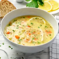 Aromatyczna zupa cytrynowa z kurczakiem, marchewką i fasolką, ozdobiona plasterkiem cytryny i natką pietruszki. Podana z chlebem.