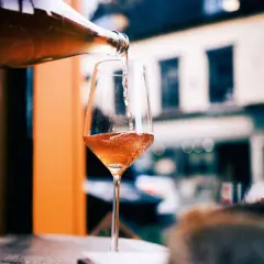 En flaska häller upp ett bubbligt, roséfärgat pet nat i ett elegant glas. En härlig kväll väntar.