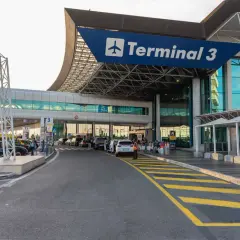 Terminal 3 lotniska Rzym Fiumicino. Samochody czekają przed wejściem, ludzie z bagażami.