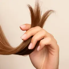 Mano sujetando mechón de cabello castaño con puntas abiertas, mostrando la necesidad de saber como reparar puntas abiertas para un cabello sano.