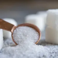 Łyżeczka z kryształkami, przypominającymi sorbitol, obok kostek cukru.