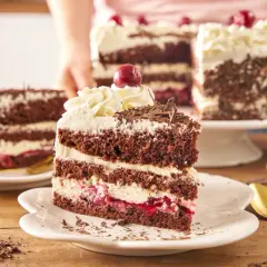 Pyszny tort szwarcwaldzki z mascarpone, przełożony kremem i wiśniami, ozdobiony czekoladowymi wiórkami i wisienką.