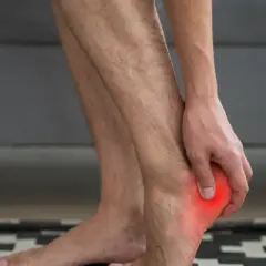Hombre tocando su talón con un punto rojo que indica dolor en el talón del pie.