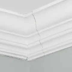 Pęknięta sztukateria w salonie, widoczna na styku ścian i sufitu.