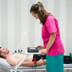 Pacjent leży na kozetce, pielęgniarka przygotowuje mu ekg spoczynkowe.