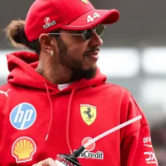 Hamilton, wielokrotny mistrz świata Formuły 1, w czerwonej bluzie z logo Ferrari i okularach przeciwsłonecznych.
