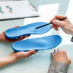 Beratung zu orthopädische einlagen kostenübernahme. Hände halten blaue Einlagen, ein Stift zeigt auf eine. Fußdruckanalyse im Hintergrund.