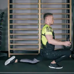 Ćwiczący wykonuje głęboki wykrok z kettlebell, co jest świetnym ćwiczeniem na mobilizację stawu skokowego.