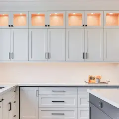 Elegante cocina moderna con gabinetes blancos, encimeras de cuarzo y detalles dorados. La iluminación cálida realza la decoración de cocinas.