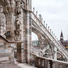 Dettaglio delle guglie e delle statue sui tetti del Duomo di Milano, con la città sullo sfondo.