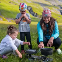 Une famille profite d'une micro aventure en famille dans un paysage montagneux verdoyant, préparant un repas en plein air.