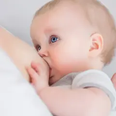 Niemowlę z niebieskimi oczami karmione piersią. Karmienie piersią może wpływać na objawy owulacji.