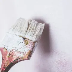 Brocha desgastada con pintura blanca lista para renovar una pared. Se puede pintar encima de pintura de caucho.