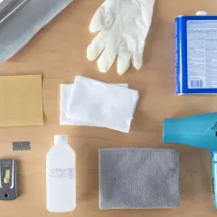 Kit pour savoir comment enlever du double face sur du carrelage : sèche-cheveux, grattoir, alcool isopropylique, gants, chiffons, papier de verre et rouleau d'aluminium.
