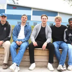 Fem unga män, potentiella k1 fighters, sitter på en träbänk framför en blå och grå byggnad.