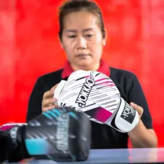A woman inspects a pair of white YOKKAO sparring gloves. Other gloves, possibly bag gloves, are visible in the foreground.