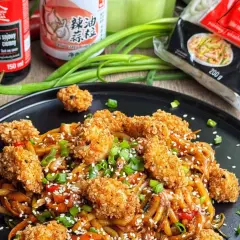 Pyszny makaron udon z kurczakiem w panierce, polany sosem sojowym, posypany sezamem i szczypiorkiem.