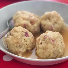 Canederli in brodo, un classico dei piatti tipici Alto Adige, serviti in una ciotola bianca su un tavolo rosso a pois bianchi.